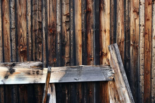 Broken wood leans against a brown-black wooden wall. The wooden wall of a wooden hut