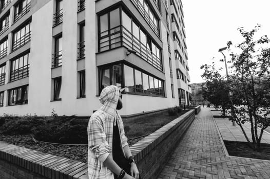 young man with beard in light checkered jacket with hood walking freely around city