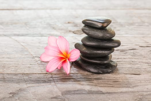 Plumeria flowers and black stones on weathered wooden background