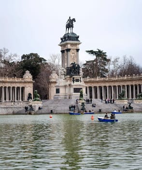 Madrid, Spain, February 2010: Equestrian monument to Alfonso XII with the lake and the tourists on the boats inside the Parque del Buen Retiro