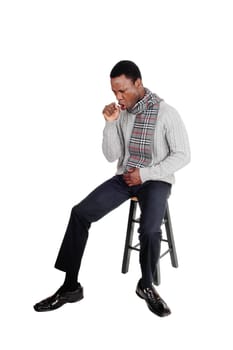 A sick African American man in a gray sweater and scarf sitting on a.chair and coughing, isolated for white background.