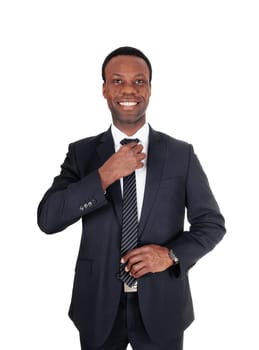 A close up image of a smiling African businessman fixing with both.hands his tie, in a dark suit, isolated for white background.
