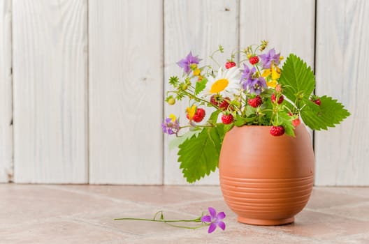 Ripe strawberries and a bouquet of forest flowers in a clay mug