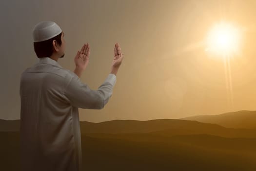Back view of asian muslim raising hand and praying with sunset background