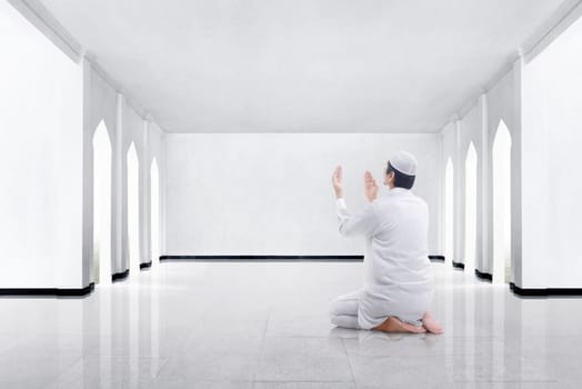 Back view of asian muslim man kneeling and praying to god in the mosque