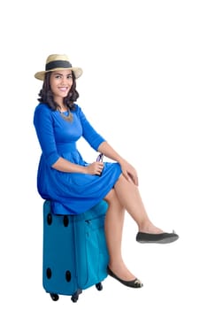 Portrait of asian woman with hat sitting on suitcase posing isolated over white background