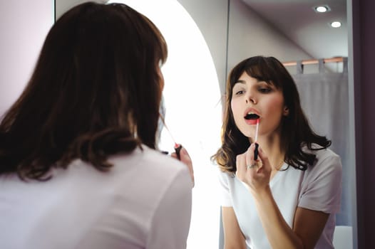 Portrait of a beautiful woman, dyes her lips lipstick pink, looking in the mirror