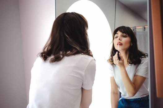 Portrait of a beautiful woman, dyes her lips lipstick pink, looking in the mirror