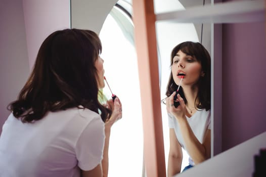 Portrait of a beautiful woman, dyes her lips lipstick pink, looking in the mirror