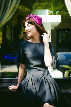 Beautiful woman in a dark stylish dress strolls along the street, near boutiques. Portrait of a fashionable girl