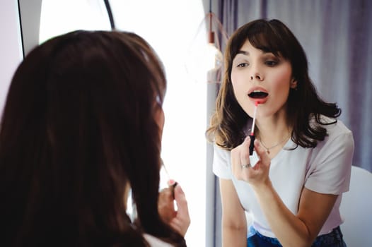 Portrait of a beautiful woman, dyes her lips lipstick pink, looking in the mirror