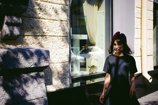 Beautiful woman in a dark stylish dress strolls along the street, near boutiques. Portrait of a fashionable girl