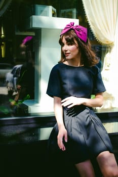 Beautiful woman in a dark stylish dress strolls along the street, near boutiques. Portrait of a fashionable girl