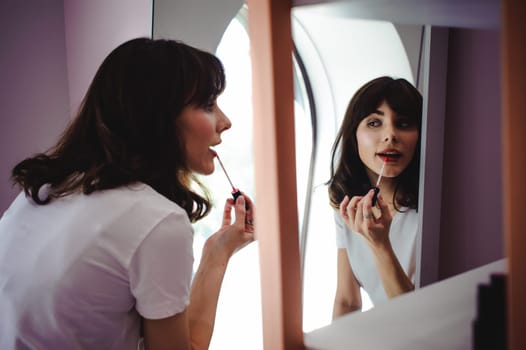 Portrait of a beautiful woman, dyes her lips lipstick pink, looking in the mirror