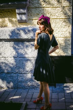 Beautiful woman in a dark stylish dress strolls along the street, near boutiques. Portrait of a fashionable girl