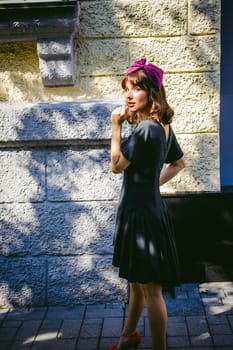 Beautiful woman in a dark stylish dress strolls along the street, near boutiques. Portrait of a fashionable girl