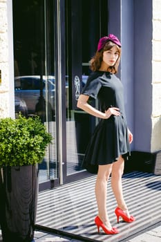 Beautiful woman in a dark stylish dress strolls along the street, near boutiques. Portrait of a fashionable girl