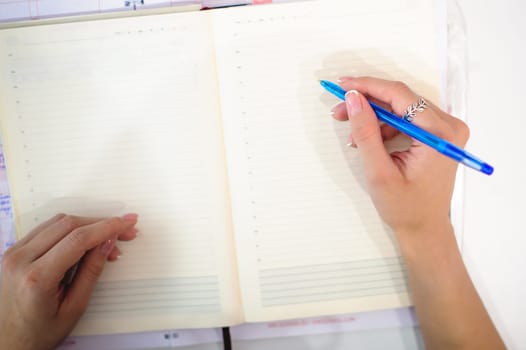 Business woman making notes in notepad. Beautiful well-groomed hands close-up hands, holding a pen, sitting in the workplace