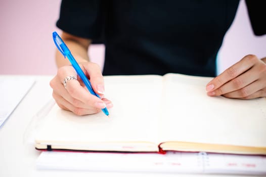 Business woman making notes in notepad. Beautiful well-groomed hands close-up hands, holding a pen, sitting in the workplace