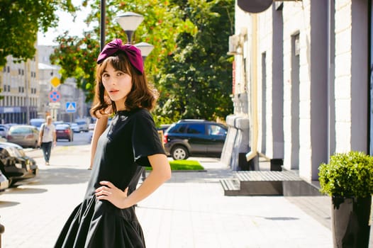 Beautiful woman in a dark stylish dress strolls along the street, near boutiques. Portrait of a fashionable girl