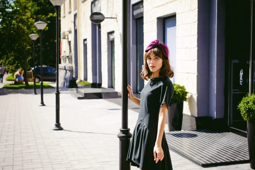 Beautiful woman in a dark stylish dress strolls along the street, near boutiques. Portrait of a fashionable girl