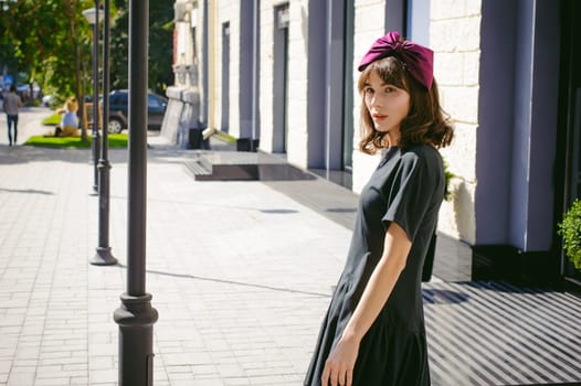 Beautiful woman in a dark stylish dress strolls along the street, near boutiques. Portrait of a fashionable girl