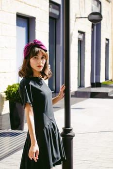 Beautiful woman in a dark stylish dress strolls along the street, near boutiques. Portrait of a fashionable girl