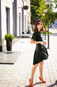 Beautiful woman in a dark stylish dress strolls along the street, near boutiques. Portrait of a fashionable girl