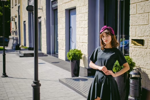 Beautiful woman in a dark stylish dress strolls along the street, near boutiques. Portrait of a fashionable girl