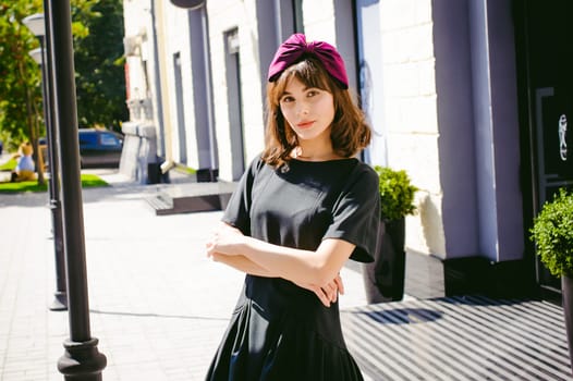 Beautiful woman in a dark stylish dress strolls along the street, near boutiques. Portrait of a fashionable girl