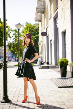 Beautiful woman in a dark stylish dress strolls along the street, near boutiques. Portrait of a fashionable girl