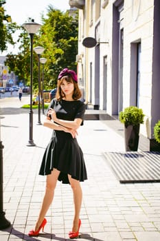 Beautiful woman in a dark stylish dress strolls along the street, near boutiques. Portrait of a fashionable girl