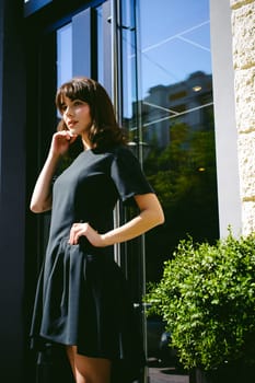Beautiful woman in a dark stylish dress strolls along the street, near boutiques. Portrait of a fashionable girl