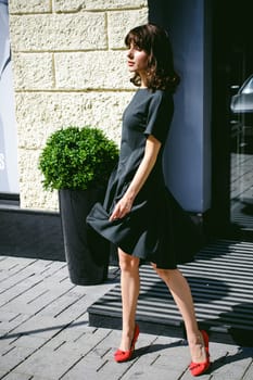 Beautiful woman in a dark stylish dress strolls along the street, near boutiques. Portrait of a fashionable girl