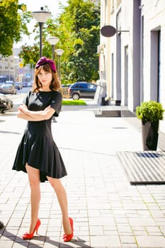 Beautiful woman in a dark stylish dress strolls along the street, near boutiques. Portrait of a fashionable girl