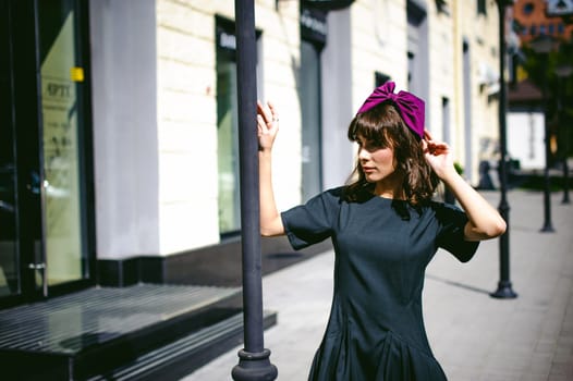 Beautiful woman in a dark stylish dress strolls along the street, near boutiques. Portrait of a fashionable girl