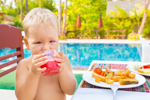 Child has a breakfast near a swimming pool