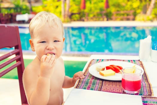 Child has a breakfast near a swimming pool