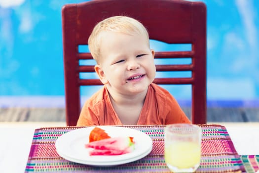 Child has a breakfast near a swimming pool