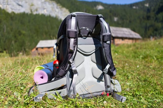 Backpack and yoga mats on mountain meadow with traditional wooden shepherd's huts, Alps, Slovenia.
