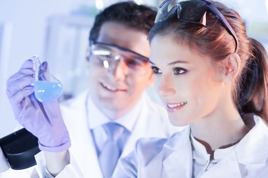Chemical laboratory. Attractive young PhD student and her post doctoral supervisor scientist observing the blue indicator color shift after the solution destillation.