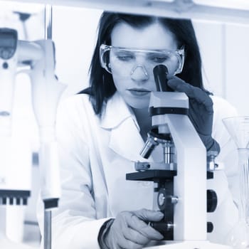 Attractive young PhD student scientist looking at the microscope slide in the life science research laboratory. Biochemistry, genetics, forensics, microbiology ..