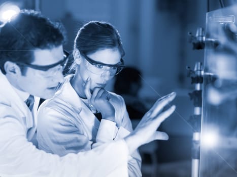 Portrait of a focused electrical engineering researchers in their working environment checking the phenomenon of breaking laser beam on the glass surface. Greyscale blue toned image.