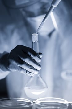 Life scientist researching in laboratory. Focused life science professional pipetting human serum media containing HIV infected cells. High protection degree work. Healthcare and biotechnology.
