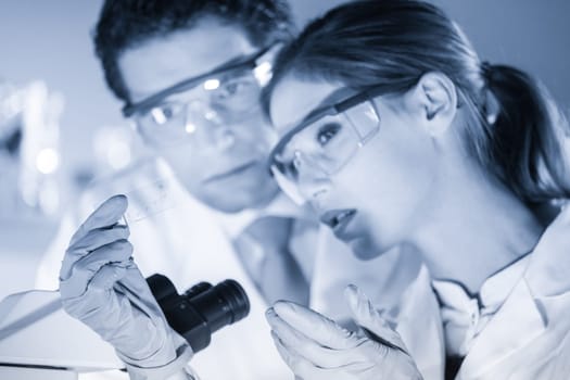 Life scientist researching in laboratory. Scientist and doctoral supervisor looking at microscope slide in forensic laboratory. Healthcare and biotechnology. Focus on slide. Greyscale blue toned.