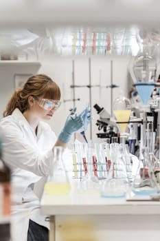 Life scientists researching in laboratory. Focused female science professional pipetting solution into glass cuvette. Lens focus on pipette. Healthcare and biotechnology.