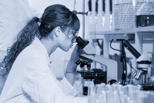 Life scientists researching in laboratory. Female young scientist microscoping in their working environment. Healthcare and biotechnology. Black and white blue toned.