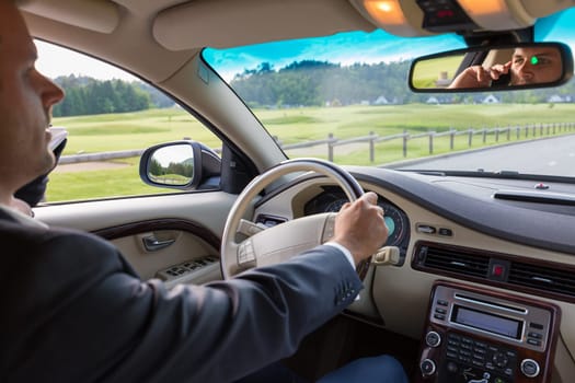 Businessman talking on cell phone while driving not paying attention to the road. Focus on the man face in rearview mirror.