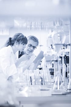 Health care professionals researching in scientific laboratory. Young female scientist and senior supervisor checking experiment protocol at tablet laptop computer in life science research laboratory.