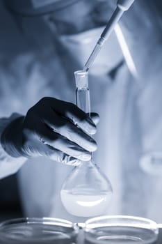 Life scientist researching in laboratory. Focused life science professional pipetting human serum media containing HIV infected cells. High protection degree work. Healthcare and biotechnology.